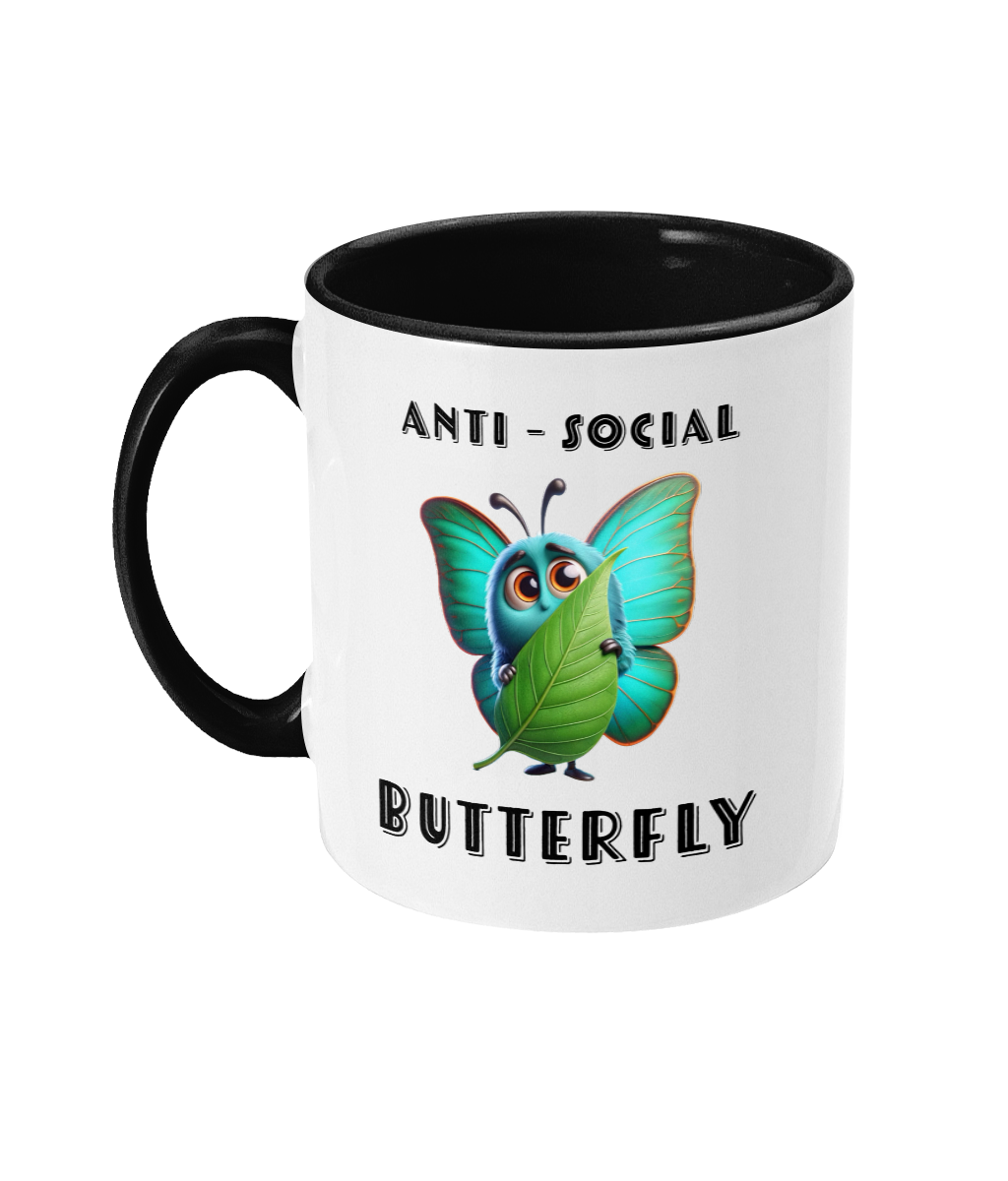  A white ceramic coffee mug with a black interior and handle, featuring the phrase “Anti-Social Butterfly” in bold, playful font. The design includes a cute, colorful cartoon butterfly holding a leaf as if hiding, adding a humorous and quirky touch.