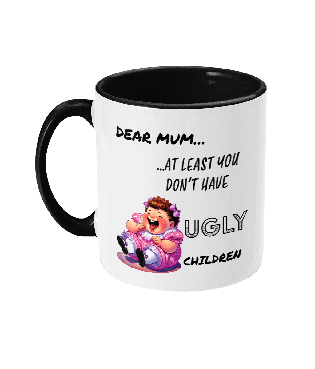 A white ceramic coffee mug with a black interior and handle, featuring the humorous text, “Dear Mum… At least you don’t have ugly children.” The design includes a colorful cartoon illustration of a laughing child in a pink dress, adding a cheeky and playful tone to the mug. The text is styled in a mix of casual and bold fonts.