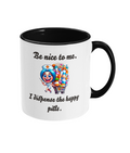 A white ceramic coffee mug with a black interior and handle, featuring the humorous text, “Be nice to me. I dispense the happy pills.” The design includes a colorful cartoon illustration of a cheerful nurse holding a syringe and standing next to a cart overflowing with colorful pill bottles, adding a playful and lighthearted touch.