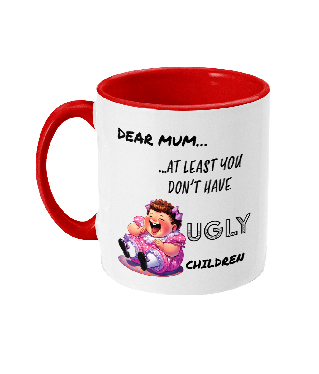 A white ceramic coffee mug with a red interior and handle, featuring the humorous text, “Dear Mum… At least you don’t have ugly children.” The design includes a colorful cartoon illustration of a laughing child in a pink dress, adding a cheeky and playful tone to the mug. The text is styled in a mix of casual and bold fonts.