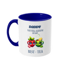  A white ceramic coffee mug with a blue interior and handle, featuring the playful phrase, “Daddy, you will always be my best-tea.” The design includes two colorful cartoon teacups with smiling faces, one red with mint leaves and a tea tag, and one green with a lemon slice and steam rising, adding a cheerful and punny touch.