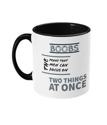  A white ceramic coffee mug with a black interior and handle, featuring the cheeky text, “Boobs: The proof that men can focus on two things at once.” The design uses bold and playful fonts, with a humorous tone, making it a lighthearted and fun gift item.