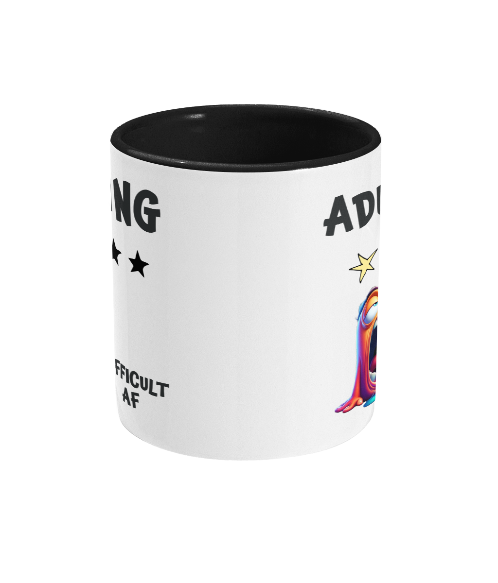  A white ceramic coffee mug with a black interior and handle, featuring humorous text that reads, “Adulting” with a 1-star rating out of 5 stars. Below the text, there’s a colorful, exaggerated cartoon character looking exhausted, with its tongue out and droopy eyes. The phrase “Difficult AF” is displayed near the bottom, adding a playful and relatable tone.